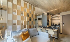 A modern living room with a sofa, a dining area with chairs, a kitchen with a counter, and a wooden partition with cut-out panels.