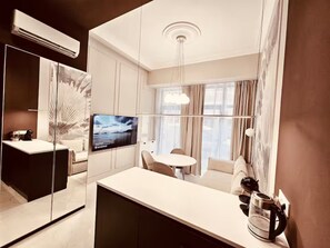 Une chambre d’hôtel moderne dotée d’un grand téléviseur à écran plat, d’un coin repas avec une table et des chaises, et d’une grande fenêtre avec des rideaux.
