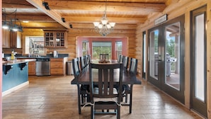 A wooden cabin interior with a dining table, chairs, a chandelier, a kitchen area, and large windows. - Fantastic 5-bedroom Cabin with Wi-Fi in Duck Creek Village  NEW LISTING (Duck Creek Village)