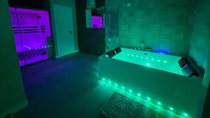 A room with a large bathtub, a door leading to another room, and a stone wall.
