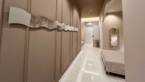 A hallway with a bed, a chair, and a door at the end.