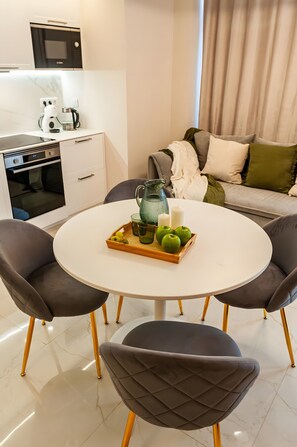 A modern kitchen with a microwave, oven, and coffee maker. There is a dining table with a tray of green apples and a candle.