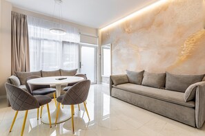 A modern living room with a round dining table, grey upholstered chairs, a grey sofa, and a marble-patterned wall.