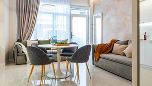 Una sala de estar moderna con un sofá, dos sillones, una mesa de centro y una zona de cocina con mostrador y armarios.