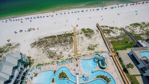Eine Vogelperspektive zeigt einen Strandort mit einem großen Poolbereich, Strandstühlen und einer Promenade.