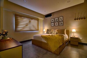 A modern bedroom with a bed, bedside tables, a window with blinds, a wall-mounted air conditioner, and framed artwork. - ®{Piantini~Views}@Downtown SD +Gym+Lounge+Pool (Santo Domingo)