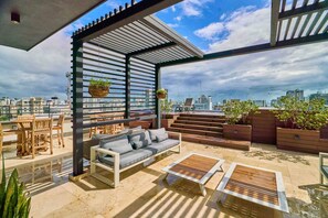 A rooftop terrace with a sofa, dining table, chairs, and potted plants. - ®{Piantini~Views}@Downtown SD +Gym+Lounge+Pool (Santo Domingo)