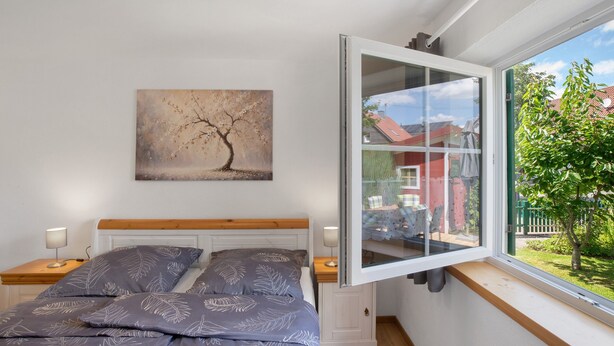 Ein Schlafzimmer mit einem Bett, zwei Nachttischen, einem Fenster mit Blick auf einen Garten und einem Bild an der Wand.