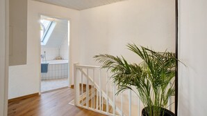 Eine Treppe mit weißer Geländer, ein Blumentopf und Blick in ein Badezimmer mit Badewanne und Fenster.