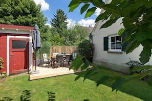 Un patio trasero con terraza de madera, un cobertizo rojo y una casa blanca con una ventana.
