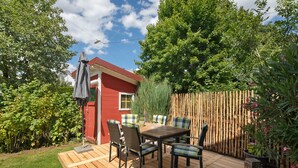 Eine Holzterrasse mit Tisch und Stühlen, umgeben von einem Holzzaun und Grünpflanzen.