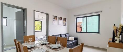A modern hotel room with a dining area, a sofa, and a large window.