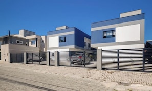 Un edificio residencial moderno de dos pisos con un camino de entrada cerrado y un coche estacionado.