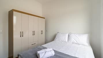Une chambre à coucher avec un lit, du linge de lit blanc, une couverture grise et une armoire.
