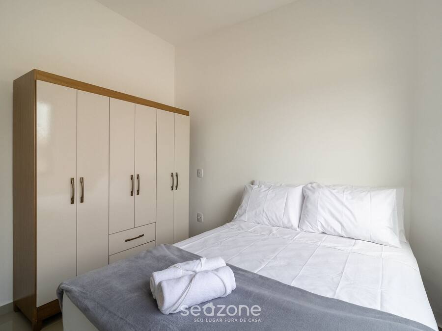 Une chambre à coucher avec un lit, du linge de lit blanc, une couverture grise et une armoire.