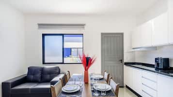 A compact living space with a dining table set for two, a sofa, a kitchen area, and a window with blinds.