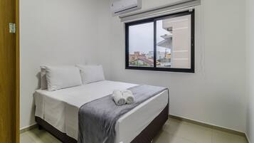 A bedroom with a bed, pillows, a window, and an air conditioner.