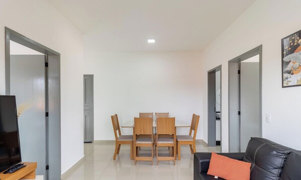 A modern living room with a dining area, featuring a flat-screen TV, a leather sofa, and a dining table with chairs. - Beautiful Apartments in Campeche - Floripa - SCO (Florianópolis)