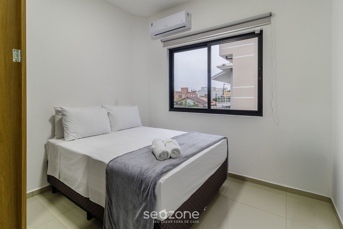 A bedroom with a bed, pillows, a window, and an air conditioner.