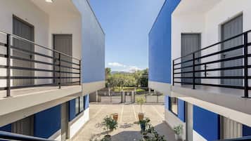 A modern building with a central courtyard, featuring balconies with black railings, potted plants, and a clear view of the surrounding landscape.