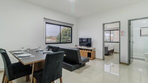 A modern living room with a dining area, a flat-screen TV, and a balcony with a view. - Beautiful Apartments in Campeche - Floripa - SCO (Florianópolis)