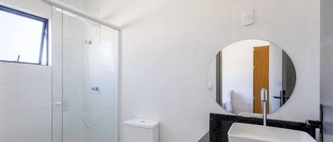 A bathroom with a toilet, sink, mirror, and shower.