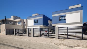 A modern residential building with a gated entrance, a paved driveway, and a clear blue sky.