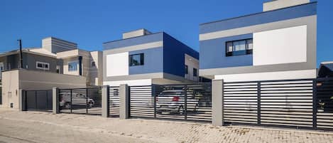 A modern residential building with a gated entrance, a paved driveway, and a clear blue sky.
