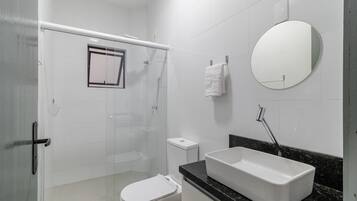 A bathroom with a shower, toilet, sink, and a mirror.
