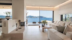 Een moderne woonkamer met een groot raam met uitzicht op water en heuvels, een bank, een bijzettafeltje en decoratieve objecten.