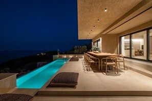 Uma área de piscina moderna ao ar livre, com espaço para refeições e vista para o mar.