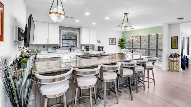 A modern kitchen with a central island, bar stools, pendant lighting, and a large window.