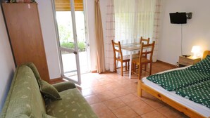 Una habitación con una cama, un sofá, una mesa con sillas, un televisor y una ventana con cortinas.