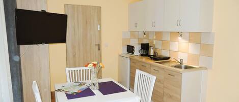 A compact kitchen with a dining area, including a table with chairs, a flat-screen TV mounted on the wall, and a microwave.