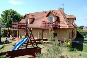 A two-story house with a red-tiled roof, a wooden deck, and a blue slide.