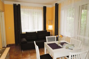 A room with a black sofa, a white table with a vase of flowers, and a lamp.