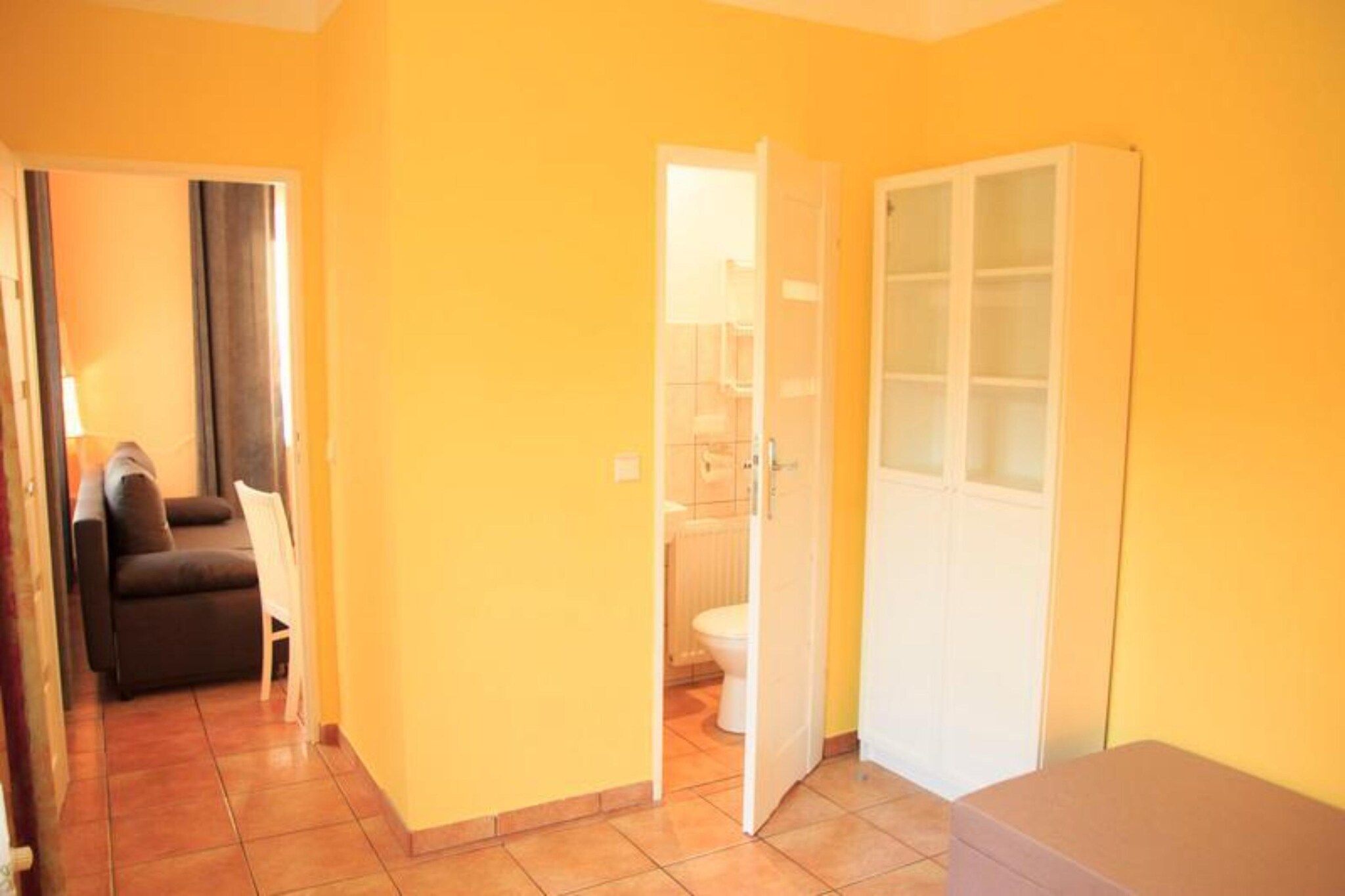 A room with a sofa, a door leading to a bathroom, and a tiled floor.