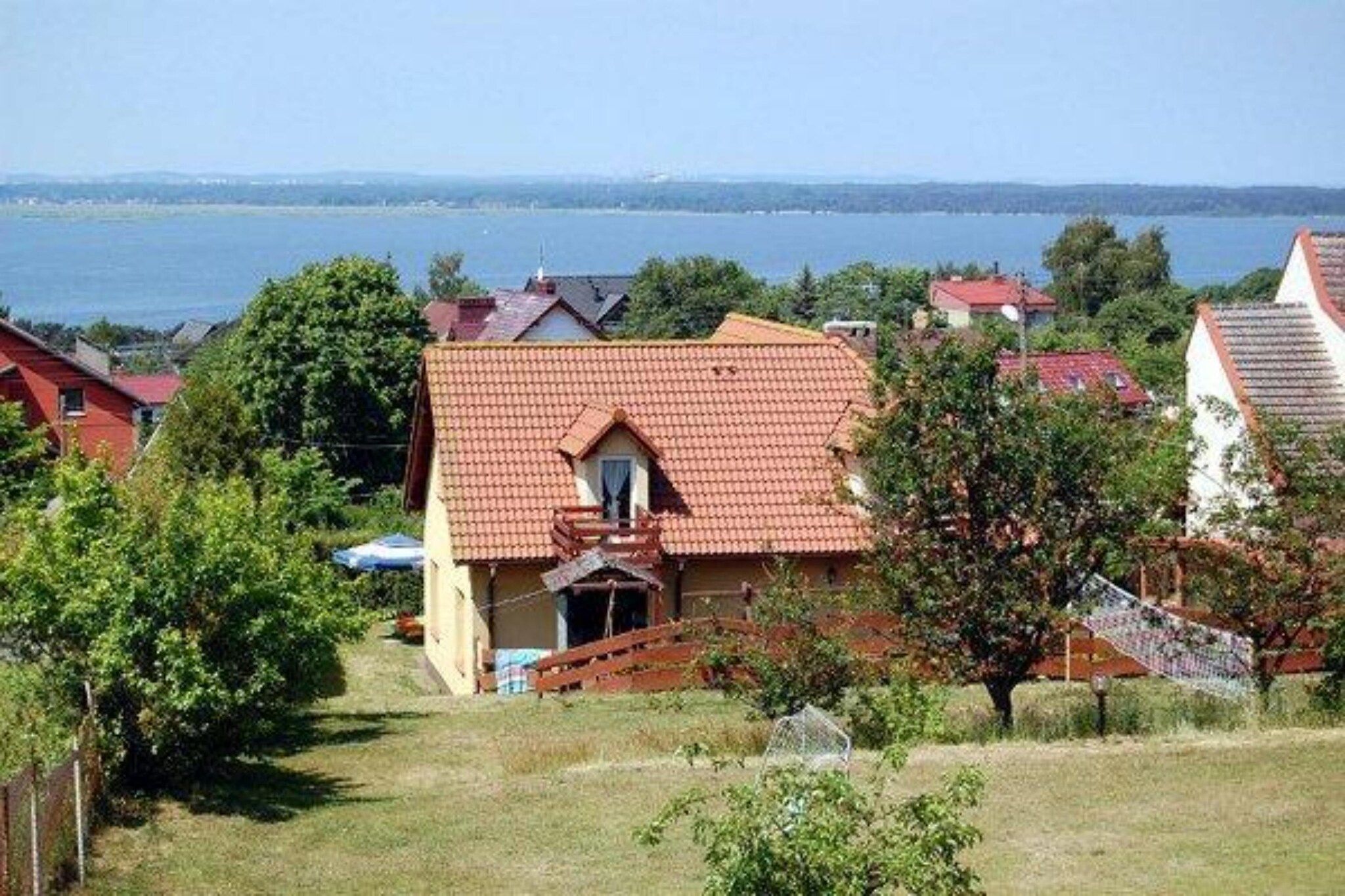A residential property with a red-tiled roof, a visible balcony, and a view of a body of water in the background.