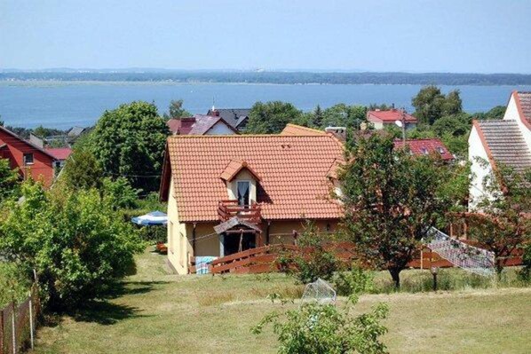 A residential property with a red-tiled roof, a visible balcony, and a view of a body of water in the background.