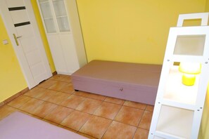 A small room with a single bed, a door, and a shelf unit.