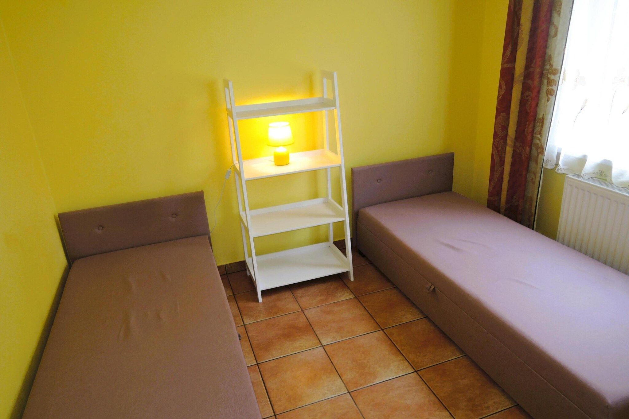 Ein kleines Zimmer mit zwei Einzelbetten, einer weißen Schrankwand und einer Lampe.