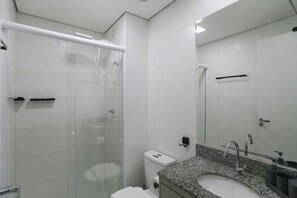 A modern bathroom with a glass shower enclosure, a toilet, a sink with a mirror, and a towel rack. - Ver.de Panorama (São Paulo)