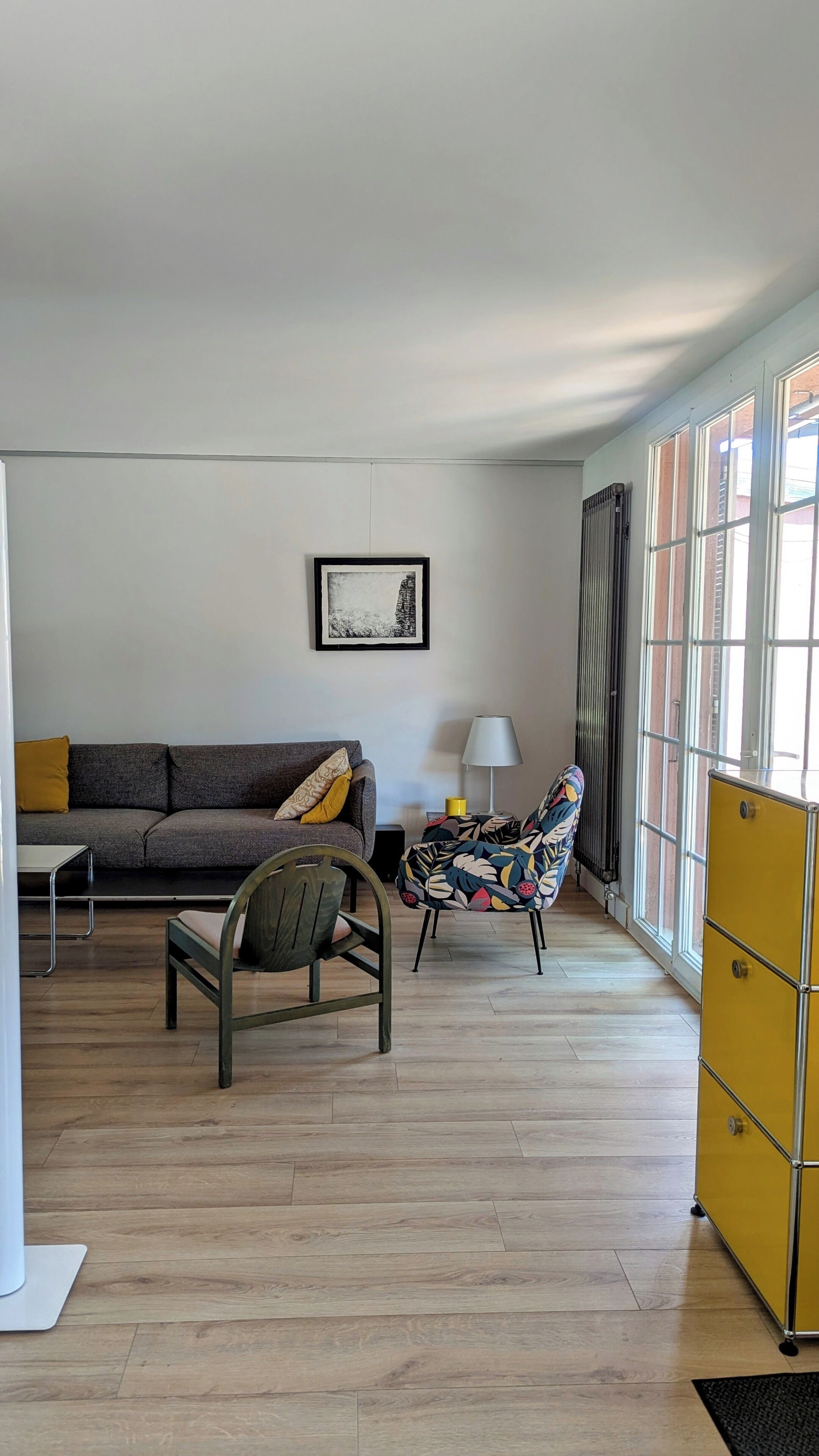 A living room with a sofa, a patterned armchair, a small table, a lamp, and a cabinet.