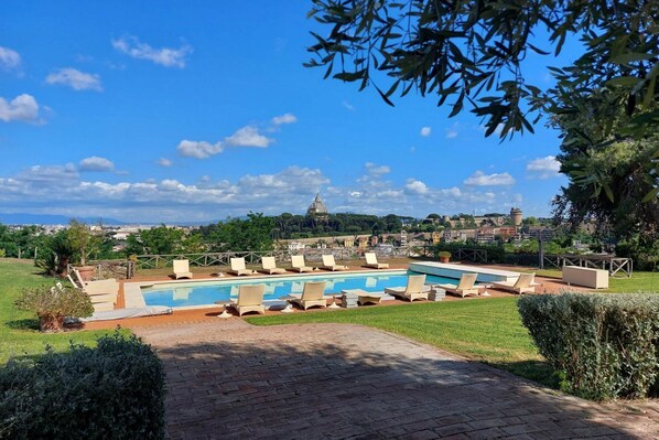 A swimming pool with lounge chairs, a brick pathway, and a view of a dome-shaped building in the distance.