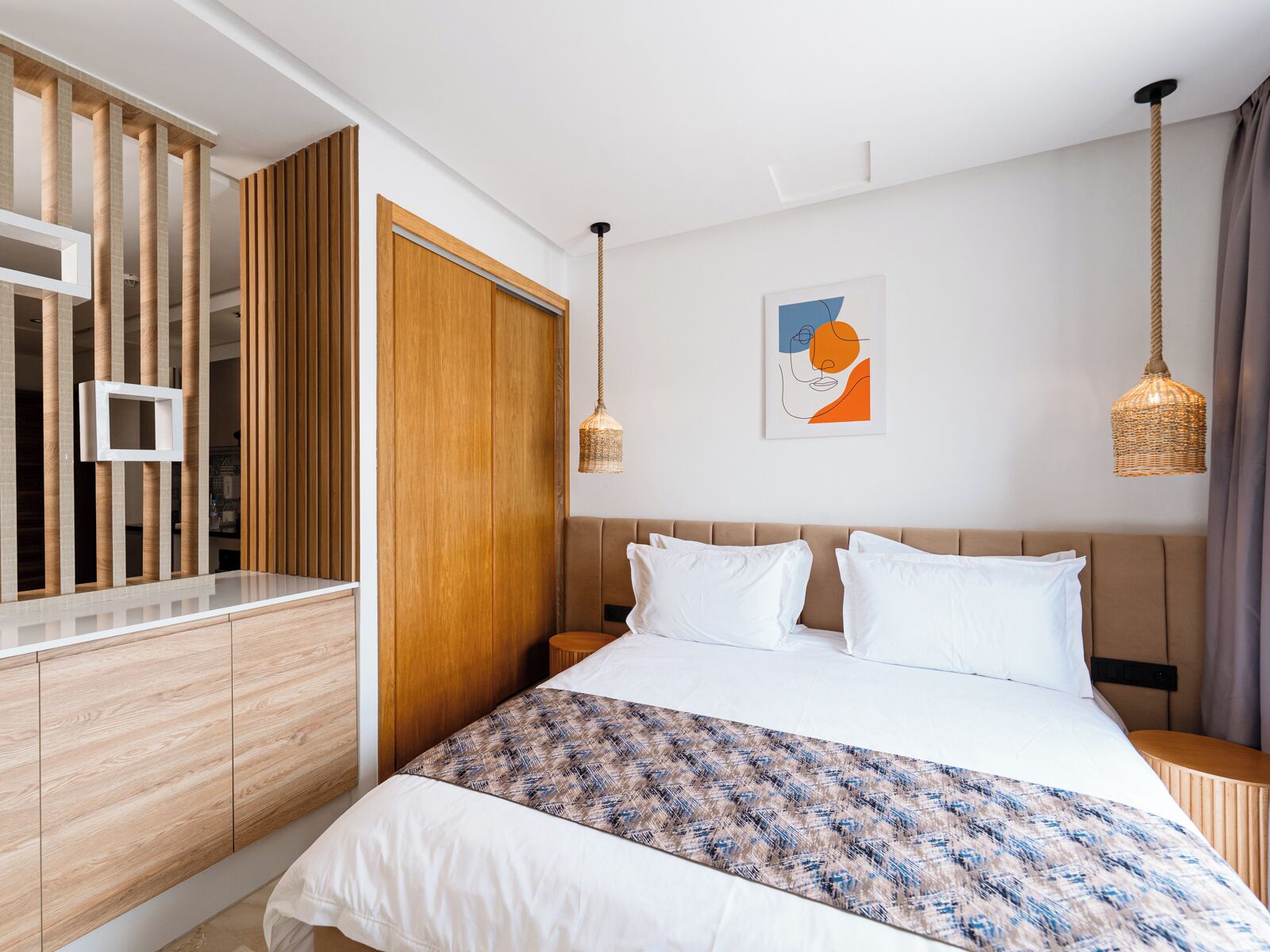 Una habitación de hotel moderna con una cama grande, un armario de madera y una obra de arte colgada en la pared.