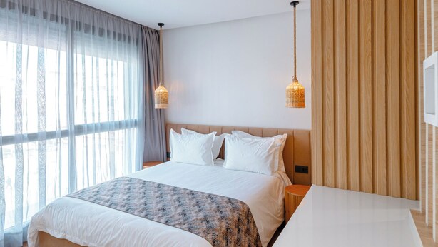 Un dormitorio moderno con una cama grande, un panel de pared de madera y un ventanal con cortinas translúcidas.