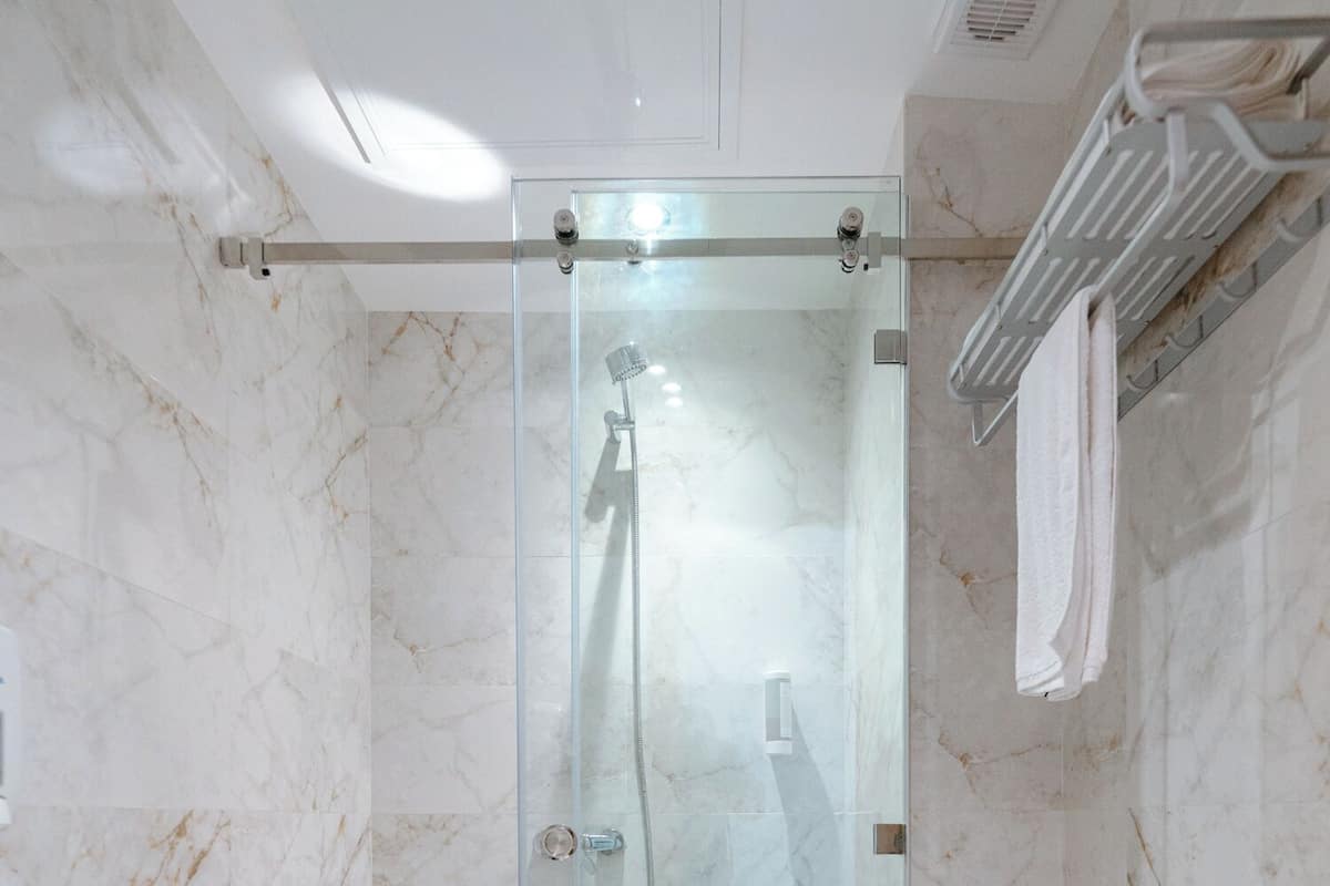 Une salle de bain moderne avec une douche à parois de verre, des toilettes blanches et un mur recouvert de carreaux de marbre.