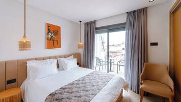 A hotel room with a large bed, a chair, a balcony with a table and chairs, and a painting on the wall.