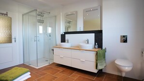 A modern bathroom with a glass shower enclosure, a double sink vanity, and a toilet.