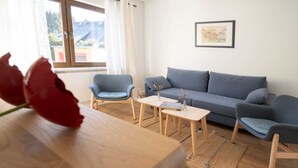 A living room with a sofa, two armchairs, a coffee table, and a wooden table with a red rose.